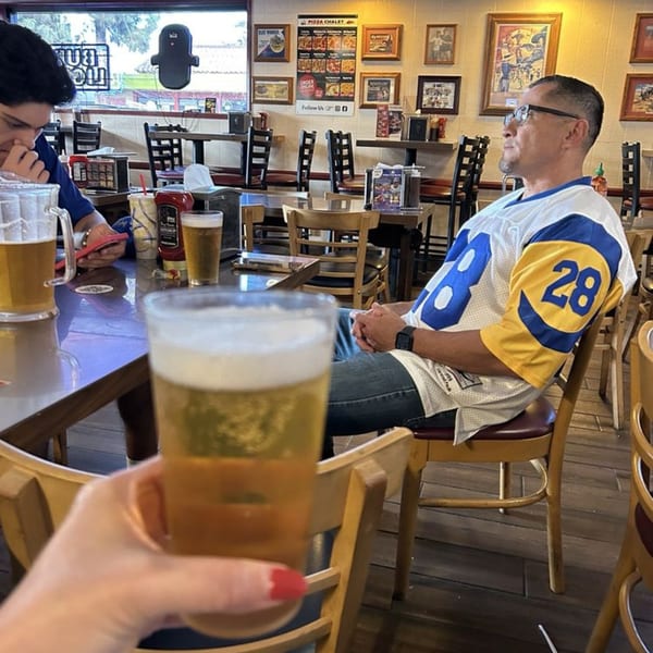 A person holding a beer glass in a restaurant with patrons, tables, and wall decor in the background.