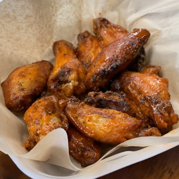 A close-up of a basket of golden-brown, saucy chicken wings from Pizza Chalet, lined with parchment paper.
