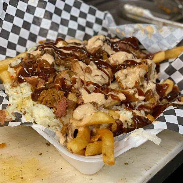 Fries topped with pulled pork, sauerkraut, BBQ sauce, and creamy dressing in a checkered paper-lined basket.