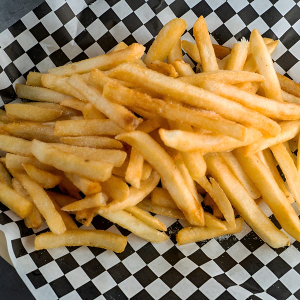 Golden-brown french fries, lightly salted, served in a black and white checkered paper basket.