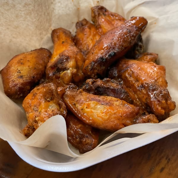 A close-up of several glistening, golden-brown chicken wings in a white paper-lined basket.