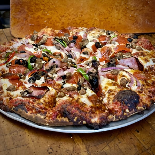 A large, sliced Pizza Chalet pizza with pepperoni, ham, sausage, olives, mushrooms, and peppers.