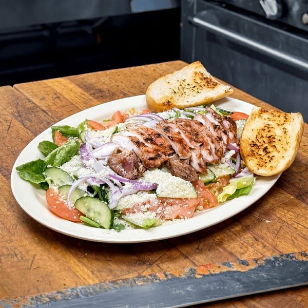 Grilled chicken salad with lettuce, tomatoes, cucumbers, red onions, feta cheese, and garlic bread.