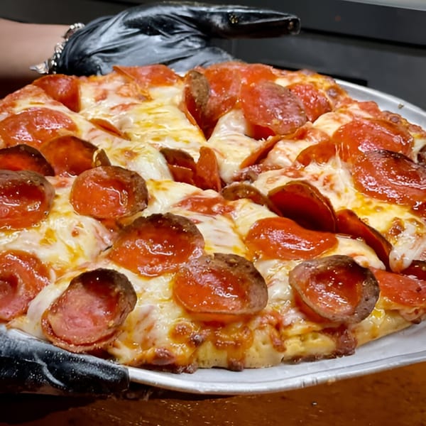 A hand in a black glove holds a freshly baked Pizza Chalet pepperoni and sausage pizza.