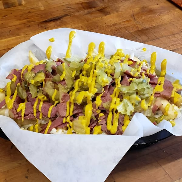 Pizza Chalet's pastrami fries, topped with sliced pastrami, pickles, and mustard drizzle.