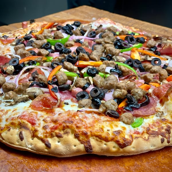 A large, fully loaded Pizza Chalet pizza with various toppings on a wooden surface.